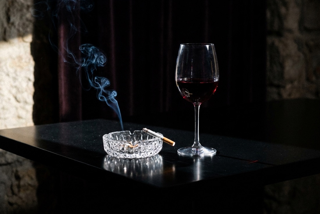 A glass of red wine beside a lit cigarette